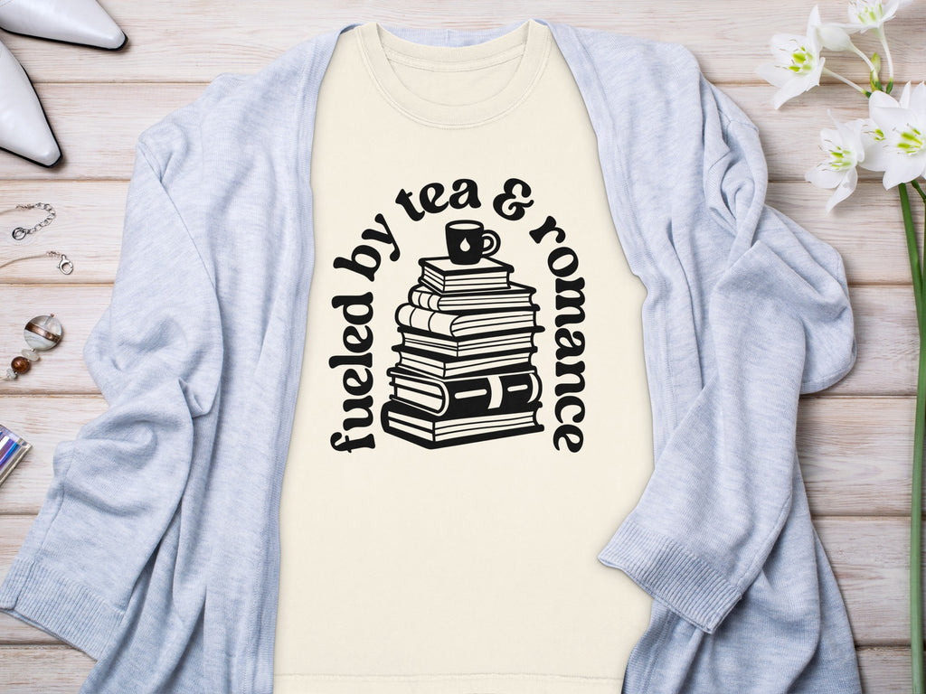 Cream t-shirt with text "Fueled by tea & romance" and stacked books graphic.