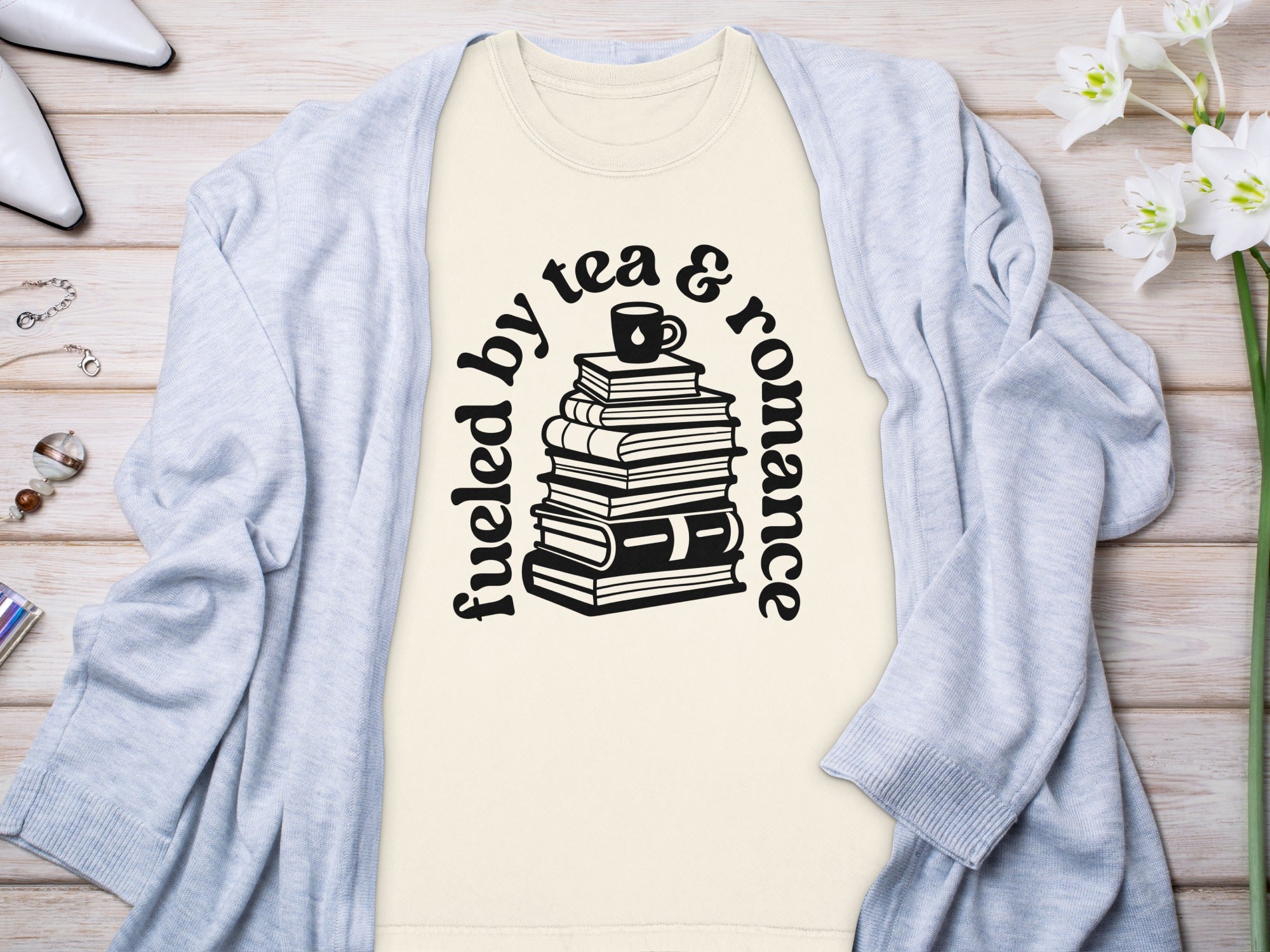 Cream t-shirt with text "Fueled by tea & romance" and stacked books graphic.