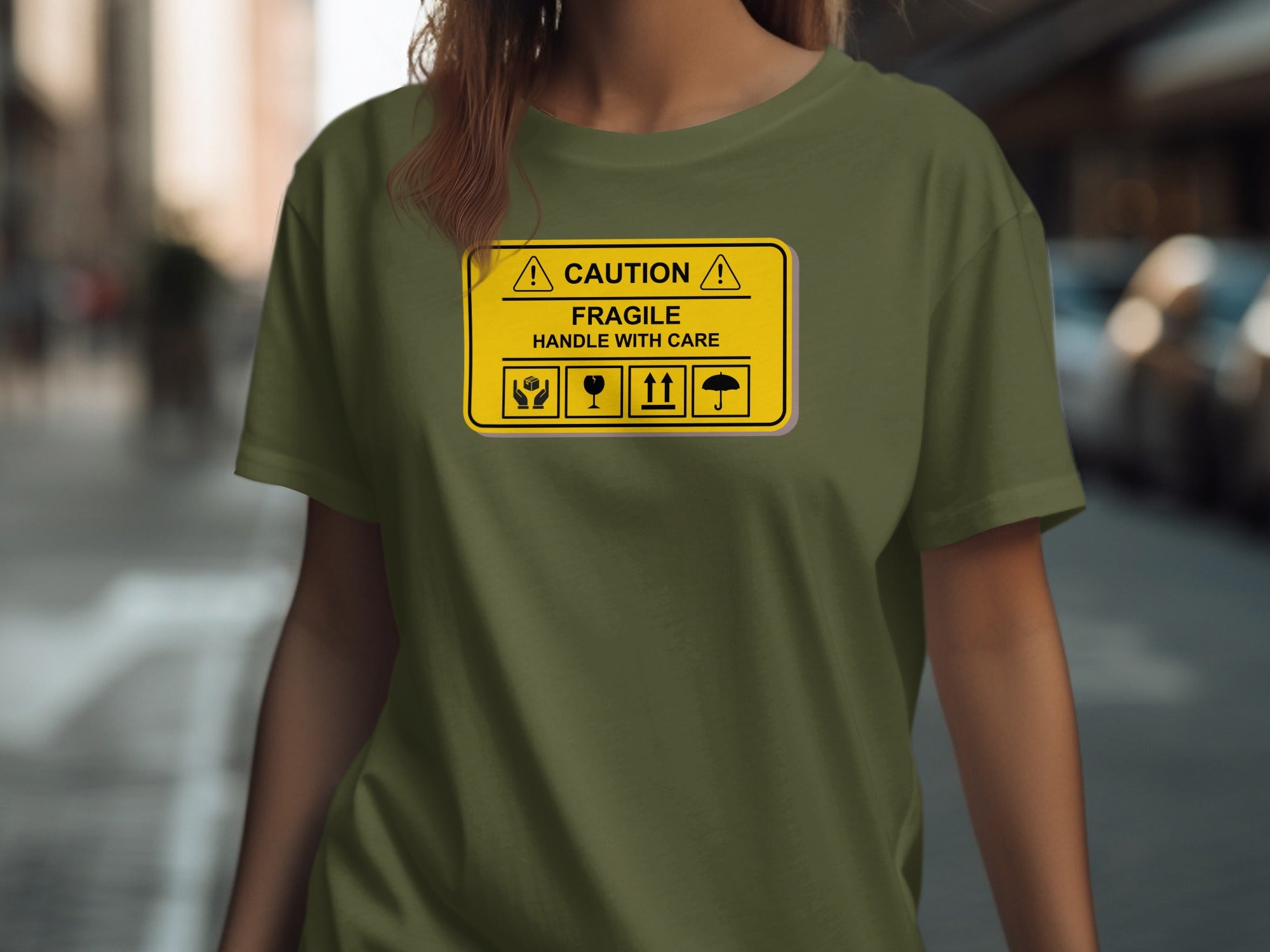 Olive green t-shirt with a yellow "CAUTION FRAGILE HANDLE WITH CARE" graphic.