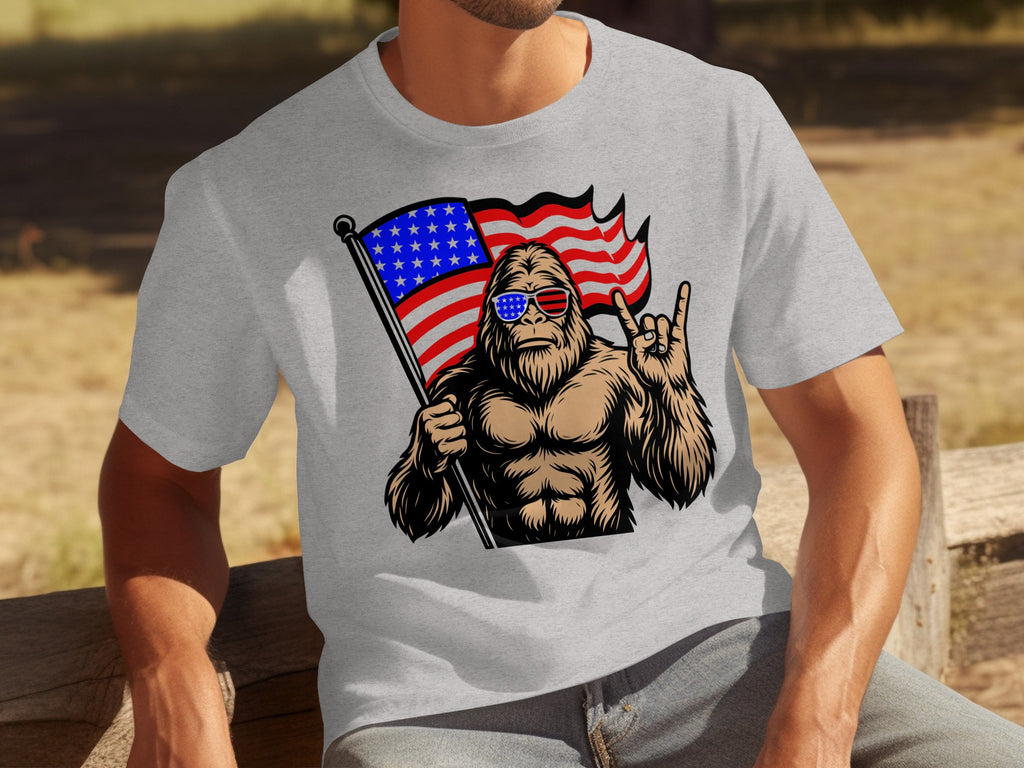 Bigfoot wearing star-spangled sunglasses holds American flag, giving rock-on hand gesture.
