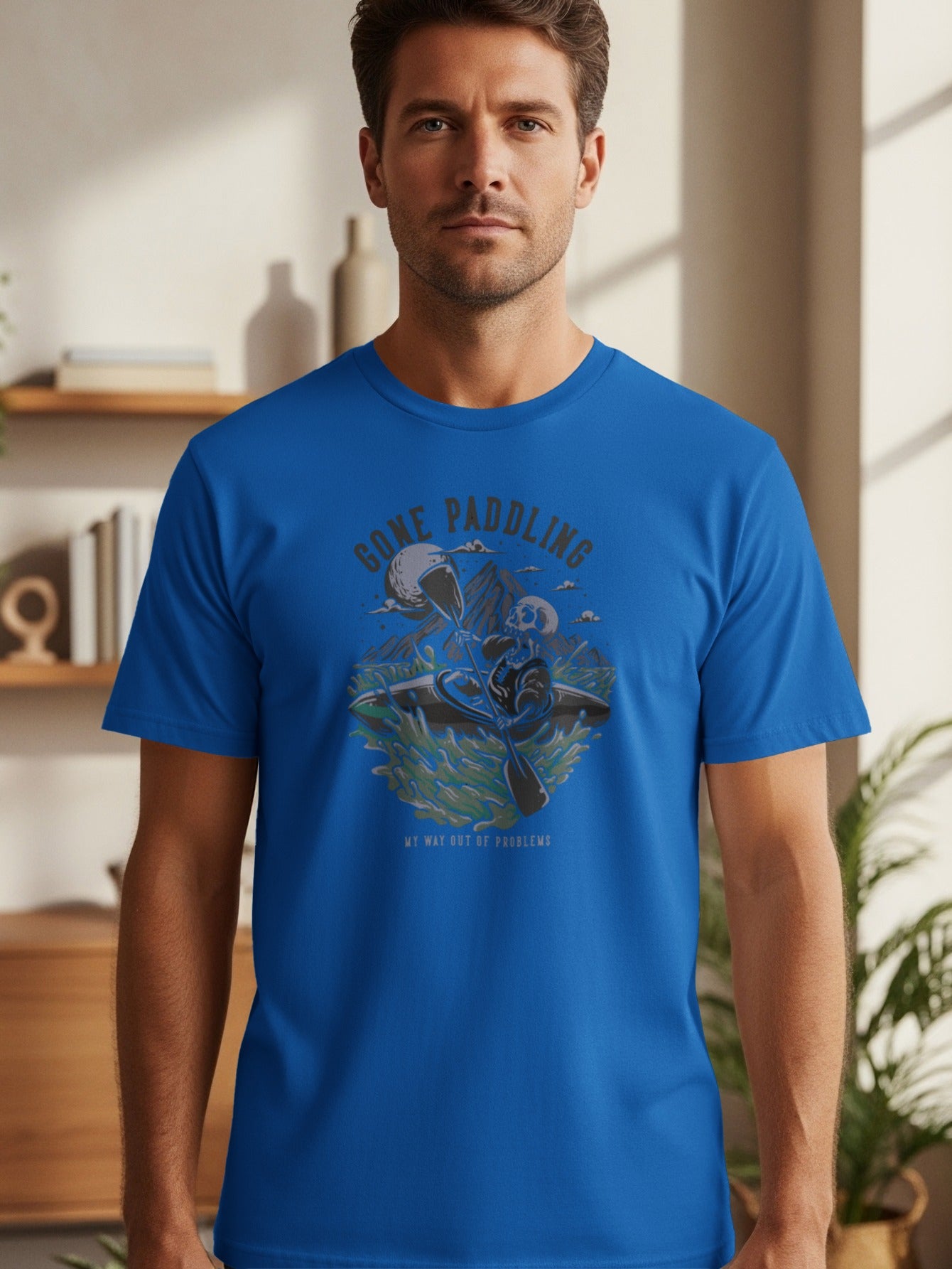 Blue t-shirt with graphic of skeleton kayaking and text "GONE PADDLING MY WAY OUT OF PROBLEMS".