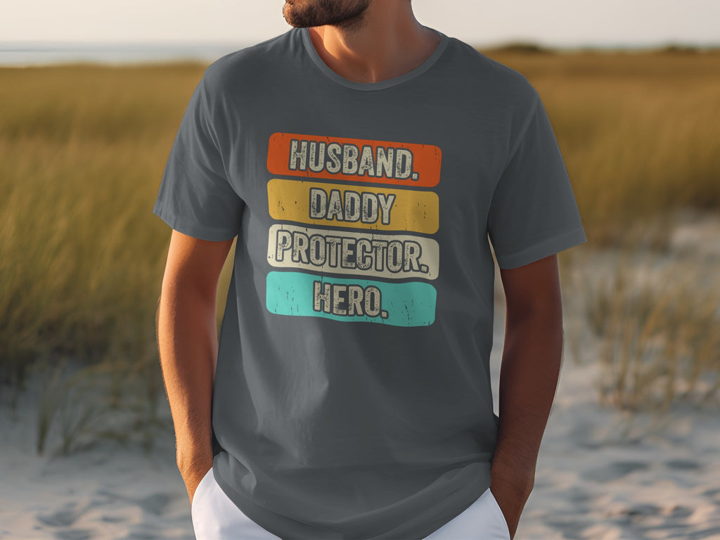Dark grey t-shirt with text "Husband. Daddy. Protector. Hero." in colorful blocks.