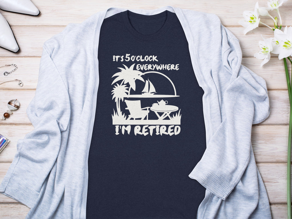 Dark blue t-shirt with white text "It's 5 o'clock everywhere I'm retired" and tropical graphic.