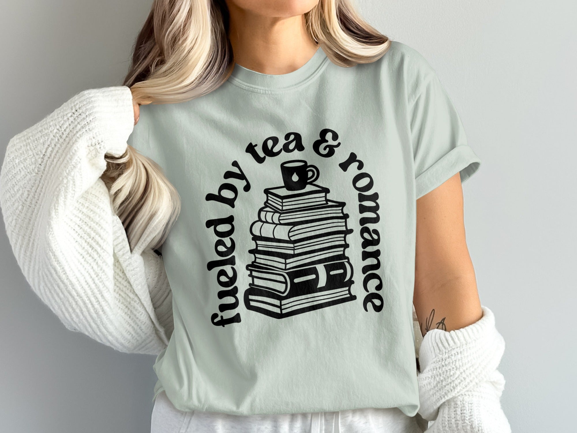 Pale green t-shirt with stack of books, cup, and text "fueled by tea & romance".