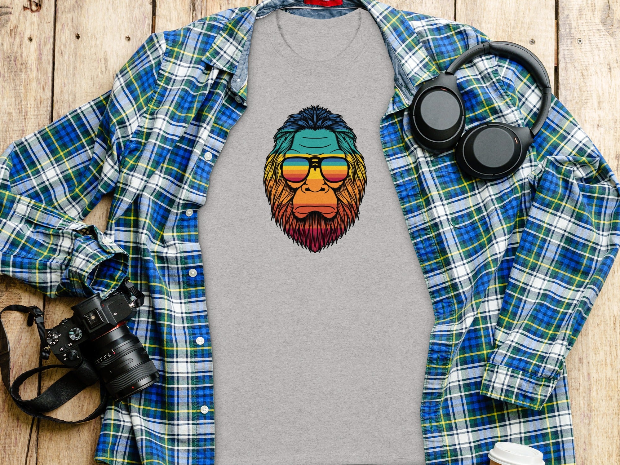 Grey t-shirt with a colorful ape graphic wearing sunglasses, laid flat with a plaid shirt.
