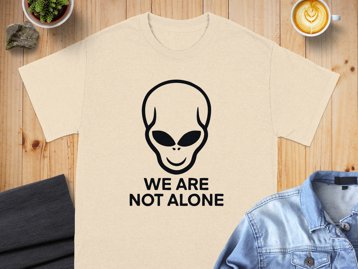 Cream t-shirt with black alien graphic and "WE ARE NOT ALONE" text.