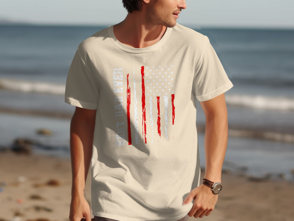 Cream t-shirt with distressed American flag graphic and text on beach background.