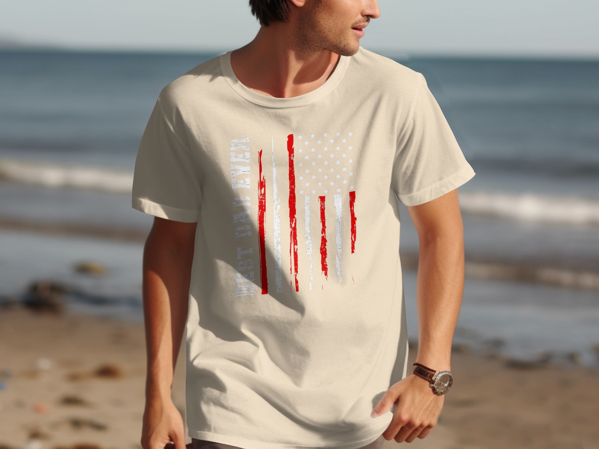 Cream t-shirt with distressed American flag graphic and text on beach background.