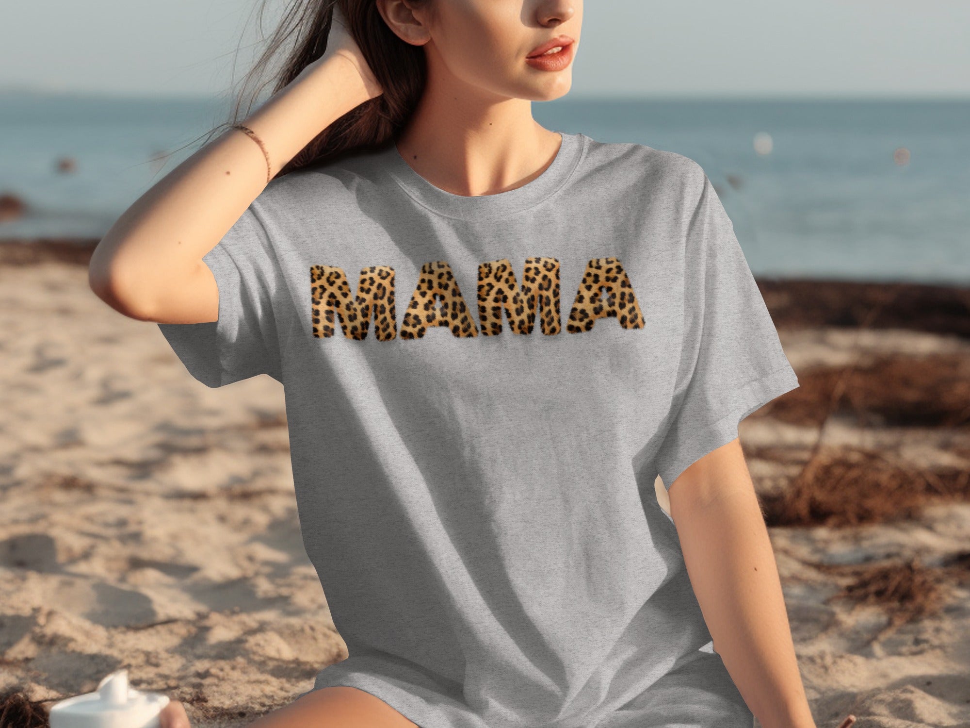 Grey t-shirt with "MAMA" in leopard print letters on a beach.