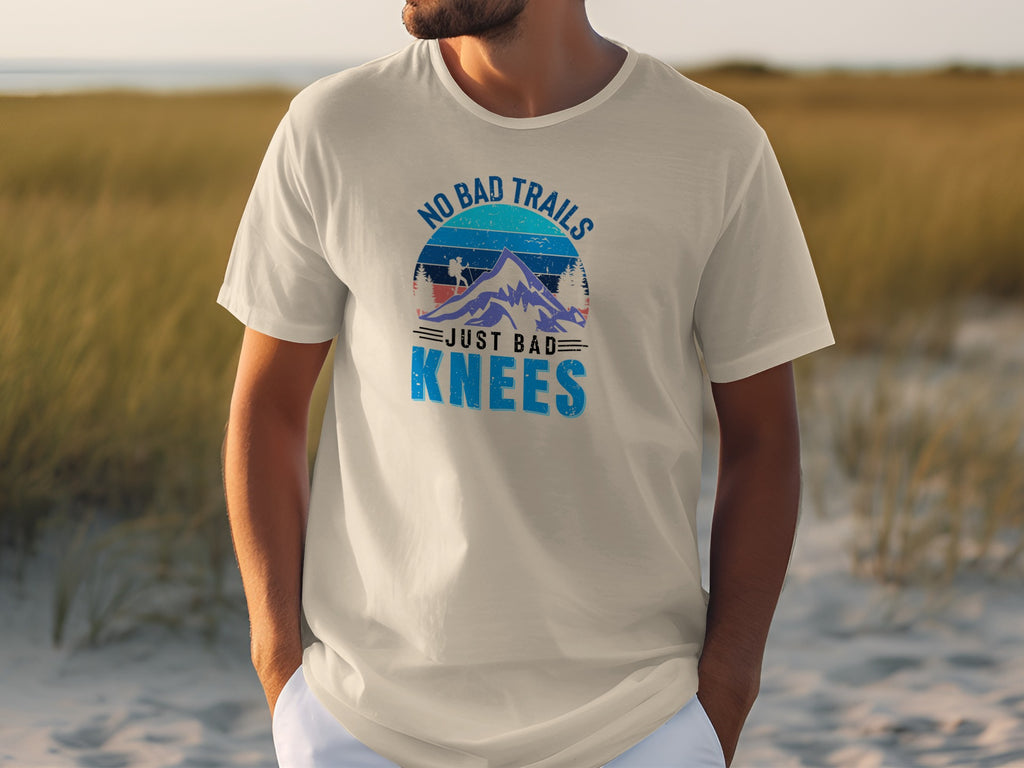 Cream t-shirt with "No Bad Trails Just Bad Knees" mountain graphic.