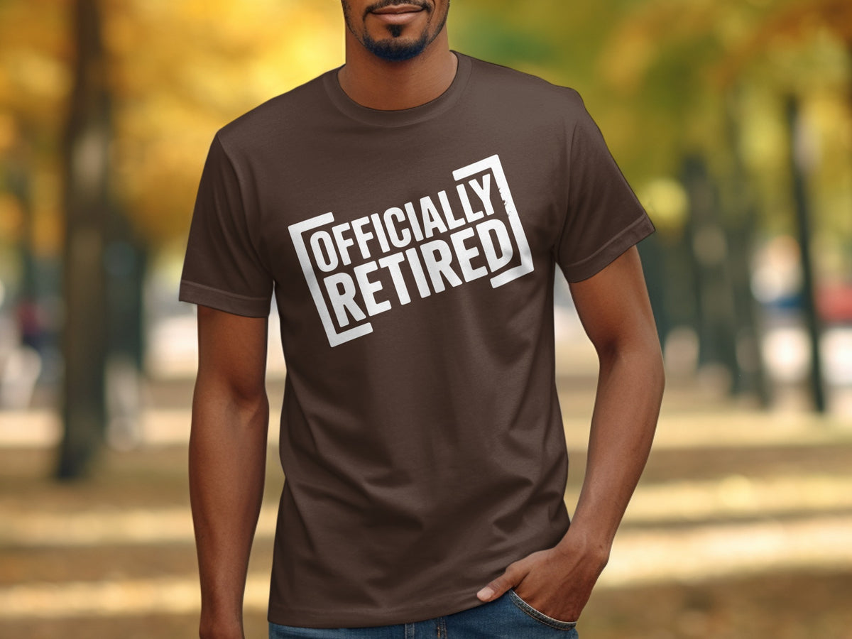 Brown t-shirt with white text "OFFICIALLY RETIRED" on a man outdoors.