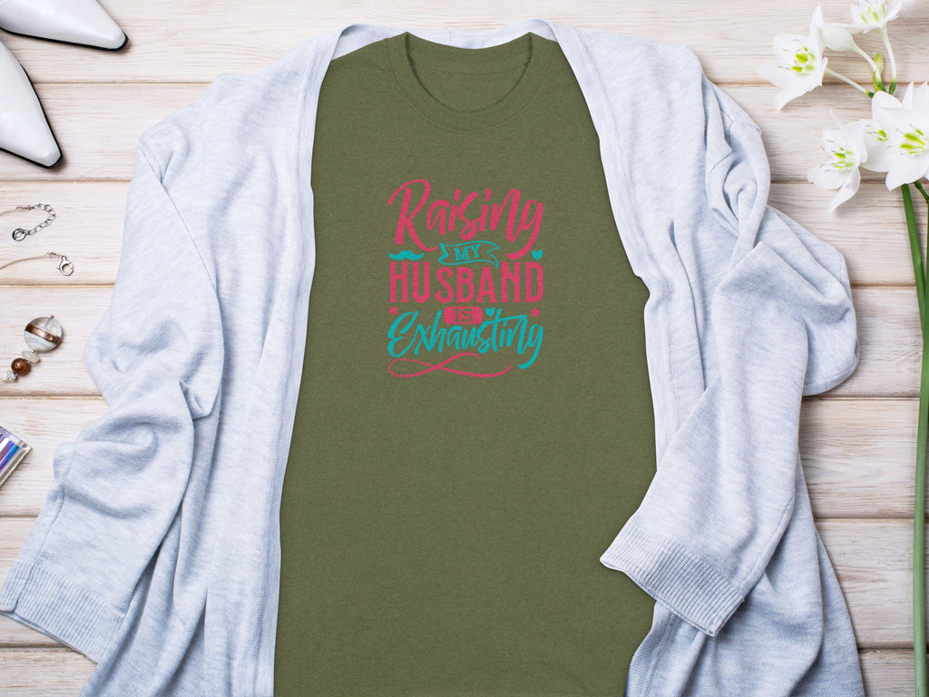Olive green t-shirt with "Raising My Husband Is Exhausting" text in pink and teal.