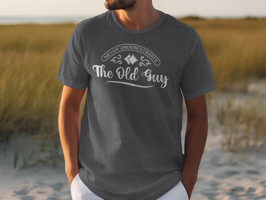 Dark grey t-shirt with white text "Never Underestimate The Old Guy".
