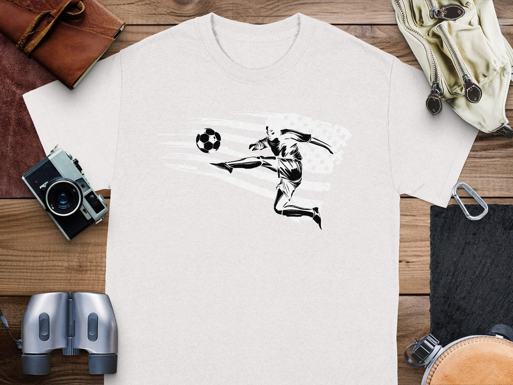 White t-shirt with black graphic of a soccer player kicking a ball, against distressed American flag.