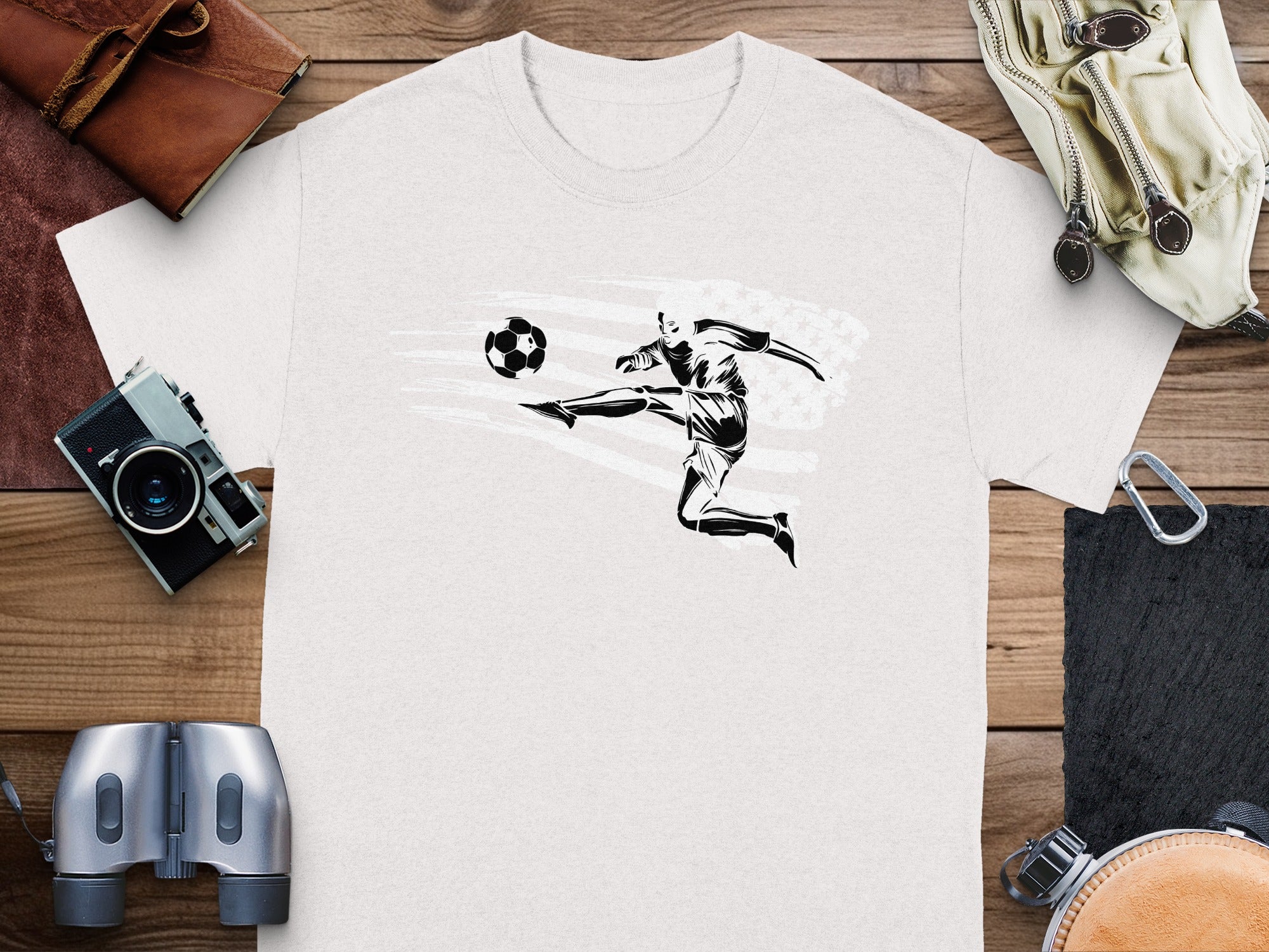 White t-shirt with black graphic of a soccer player kicking a ball, against distressed American flag.