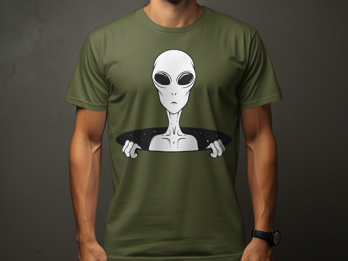 Olive green t-shirt with a graphic of a white alien peering from a circular hole in space.