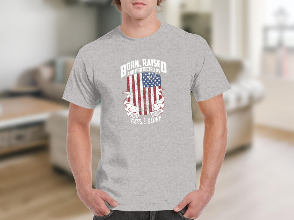 Gray t-shirt with distressed American flag and text "Born, Raised, and Protected By God, Guts, Guns, Glory".