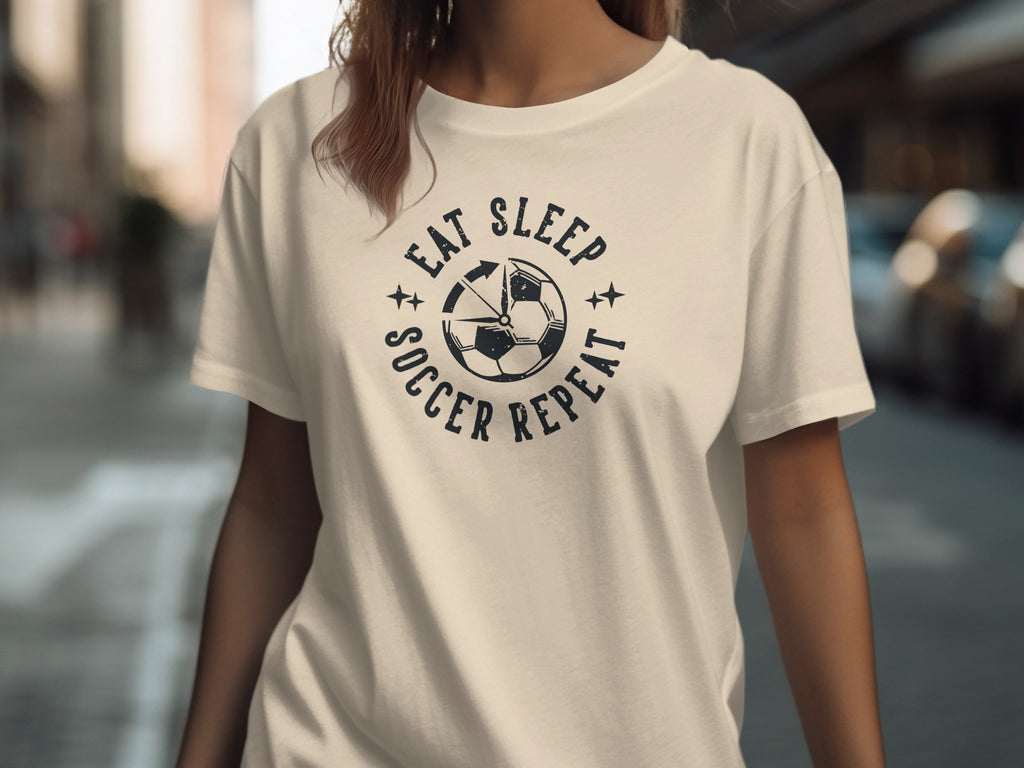 Cream t-shirt with black "Eat Sleep Soccer Repeat" graphic and soccer ball.