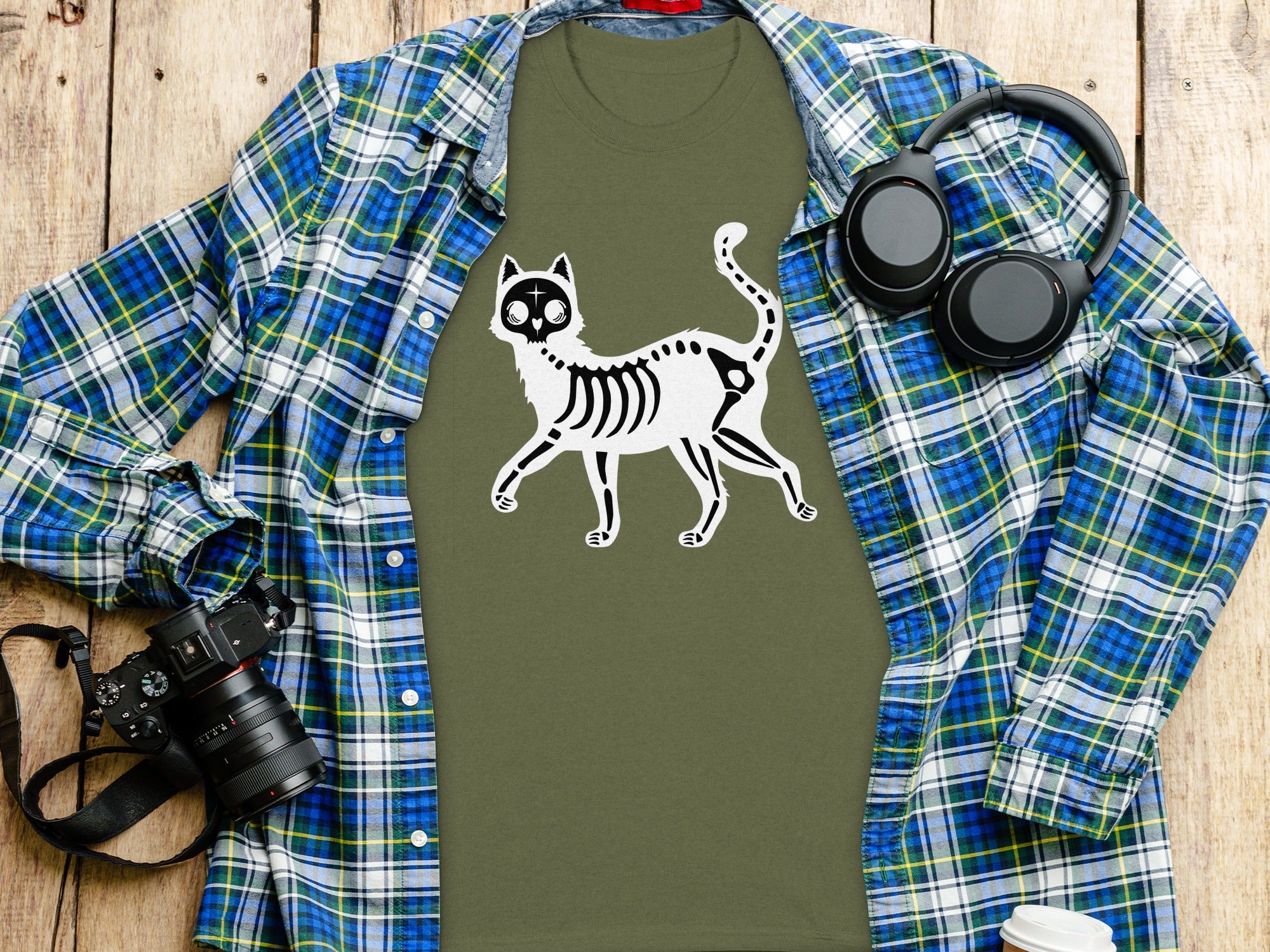 Olive green t-shirt with a white skeleton cat graphic, layered with a plaid shirt.