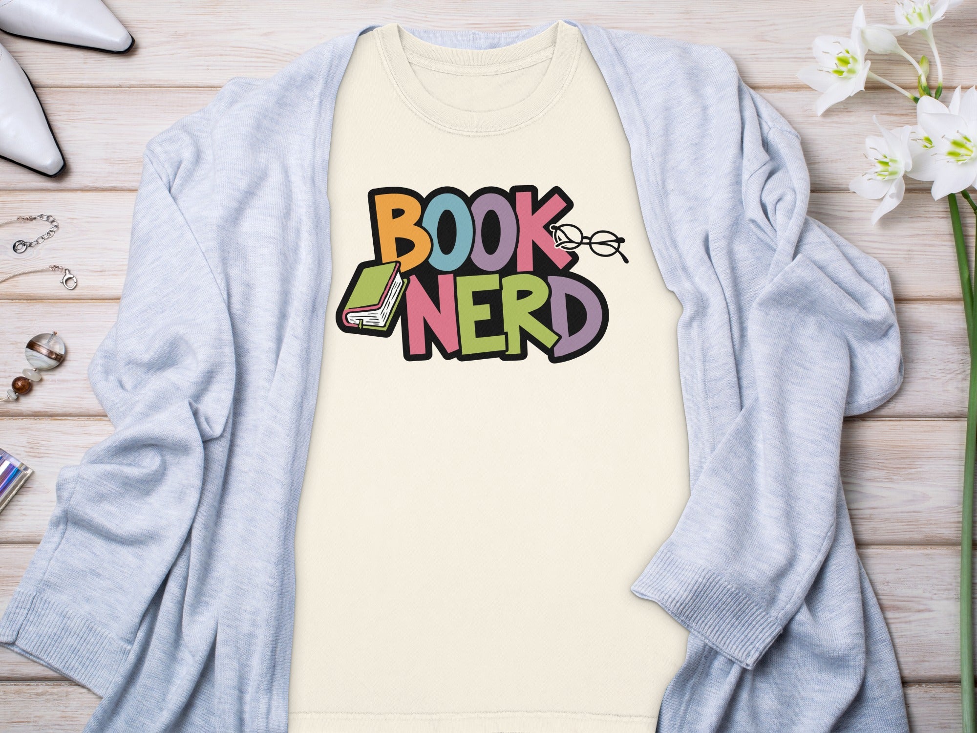 Cream t-shirt with colorful "BOOK NERD" text, glasses, and book graphic.