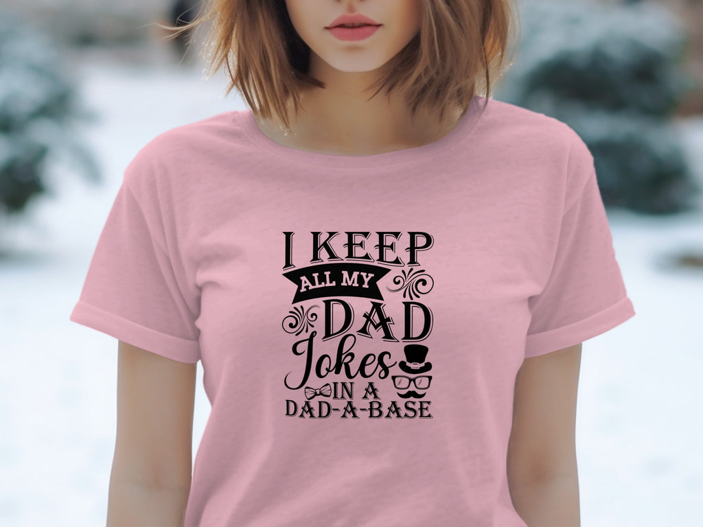 Pink t-shirt with black text: "I KEEP ALL MY DAD Jokes IN A DAD-A-BASE".