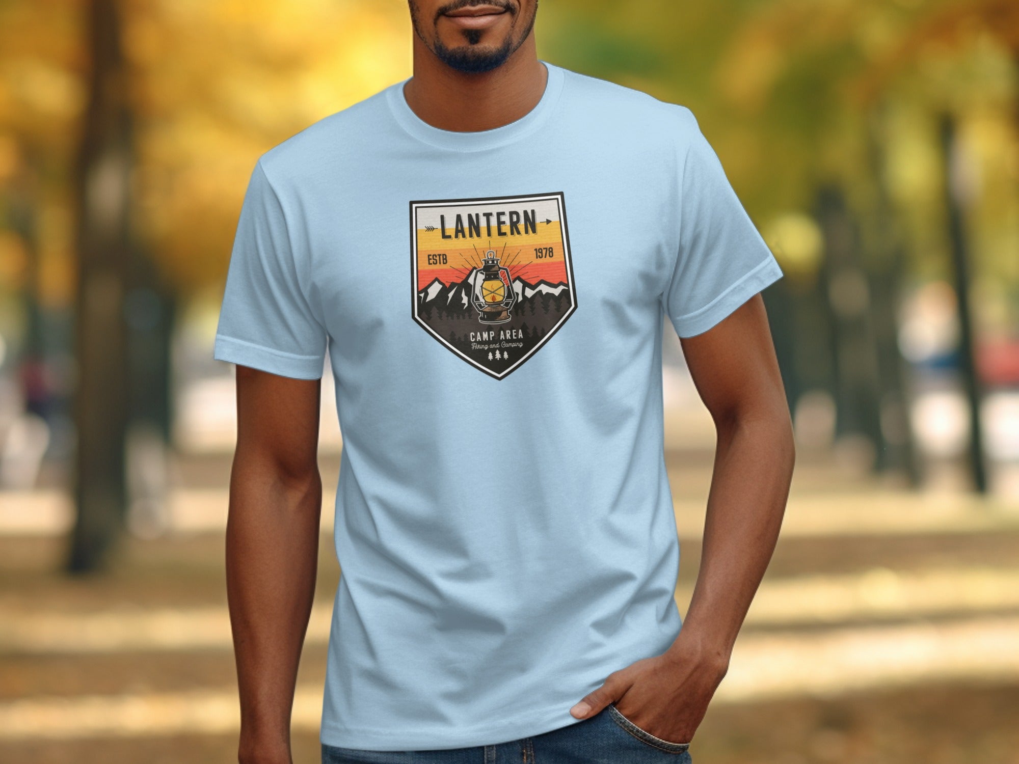 Light blue t-shirt with a distressed badge graphic featuring a lantern and mountains.