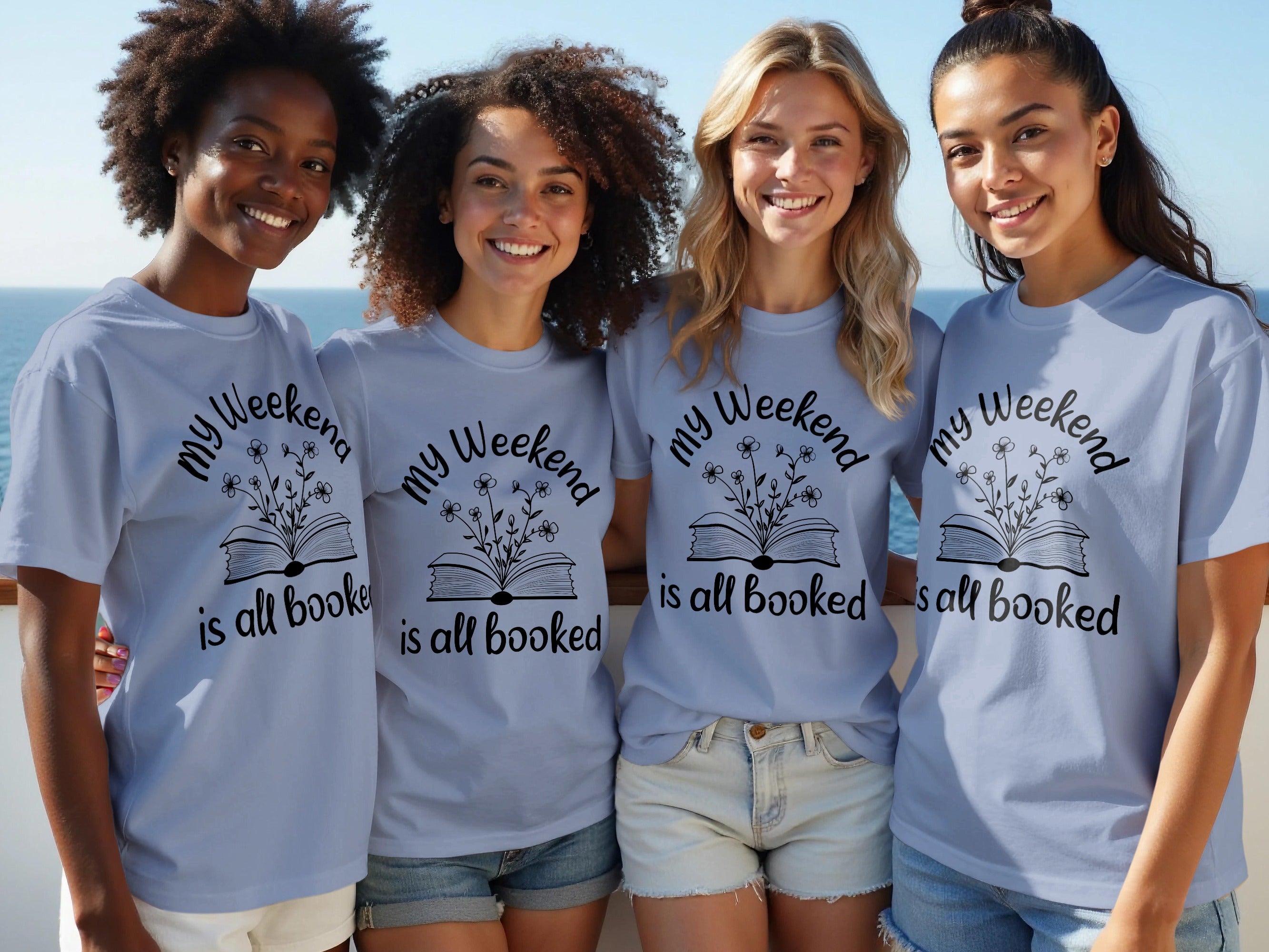 Four women smile wearing light blue t-shirts with a book and flower design.