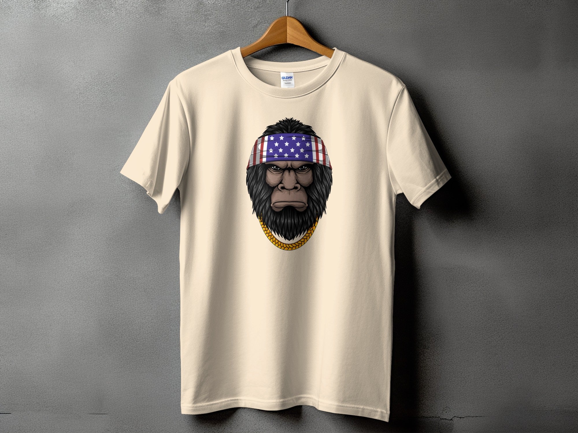 Cream t-shirt with a Bigfoot head wearing an American flag bandana and gold chain.