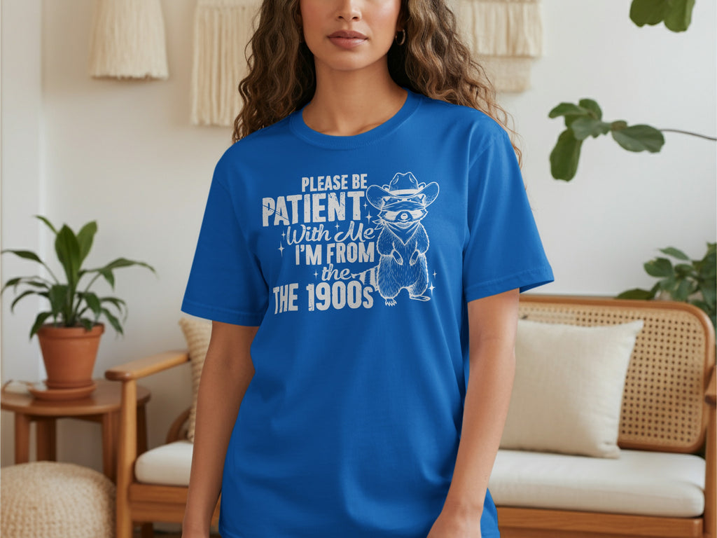 Blue t-shirt with raccoon in cowboy hat saying "Please Be Patient With Me I'm From The 1900s."