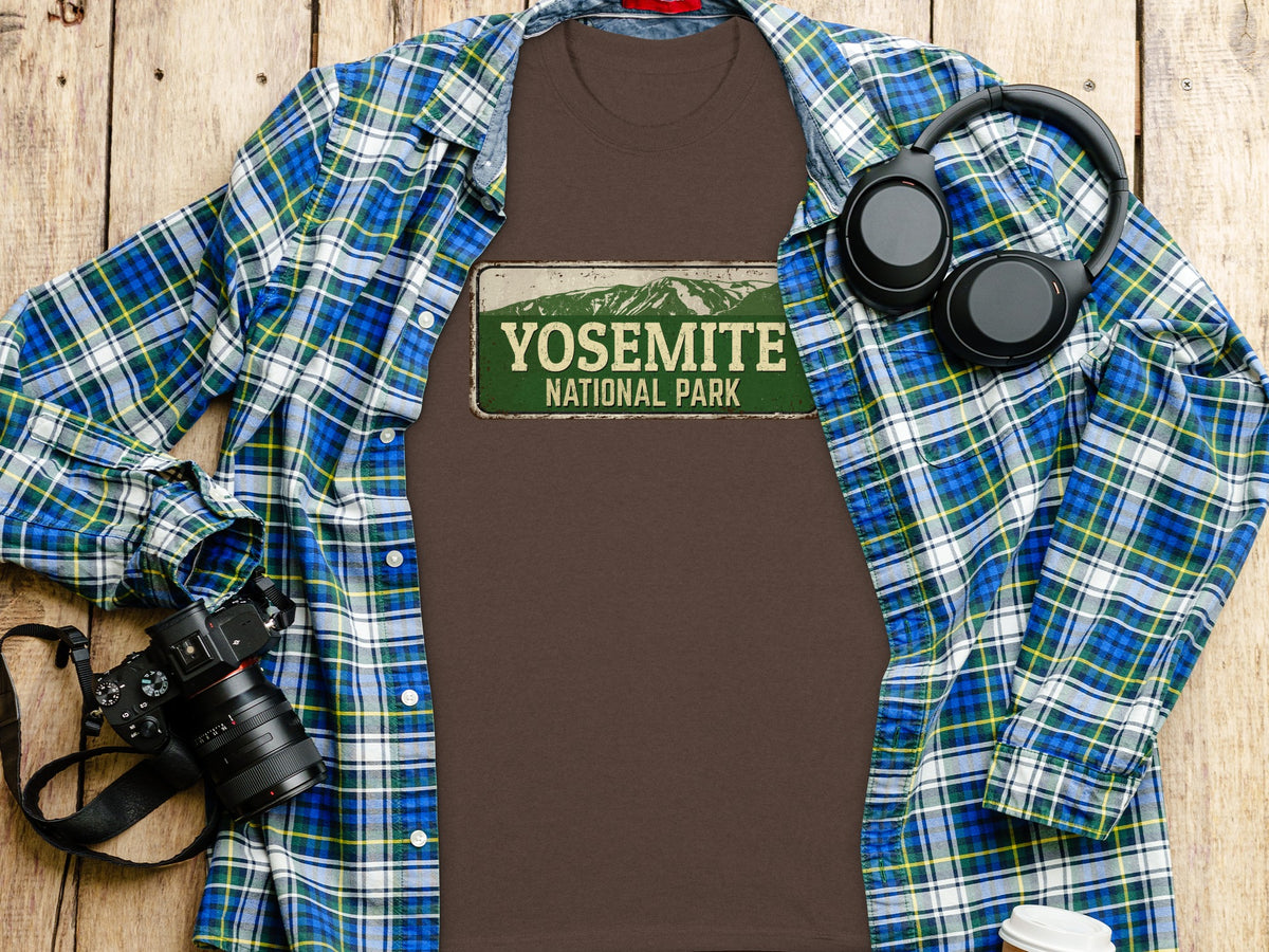 Brown t-shirt with Yosemite National Park graphic, open plaid shirt, camera, and headphones.