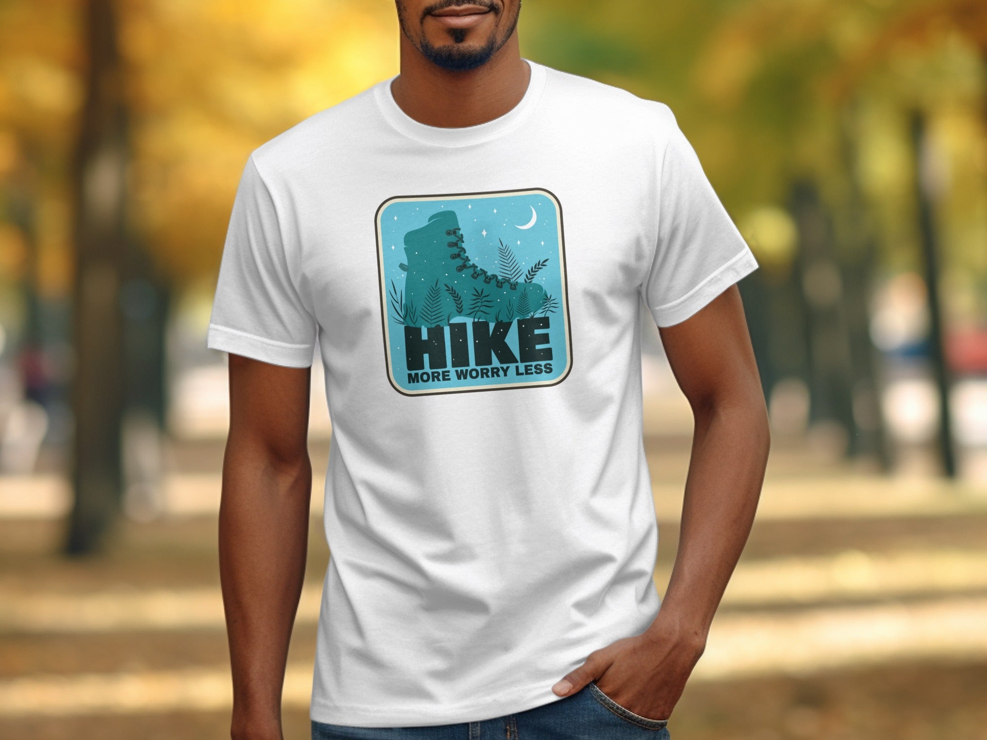 White t-shirt graphic with teal silhouette of hiking boot, foliage, moon, and text "Hike More Worry Less".