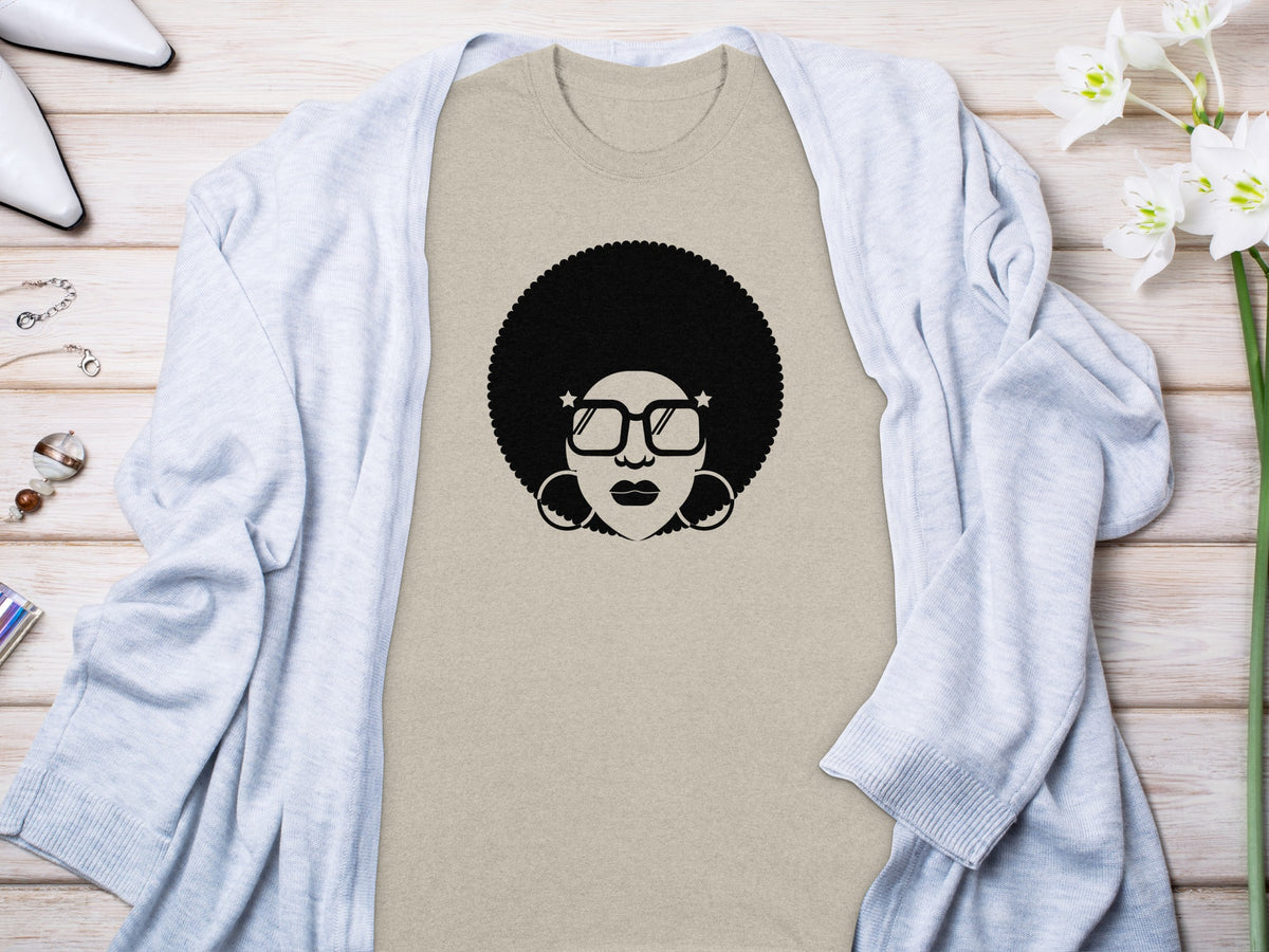 Tan t-shirt with a black graphic of a woman with an afro and star-shaped glasses.