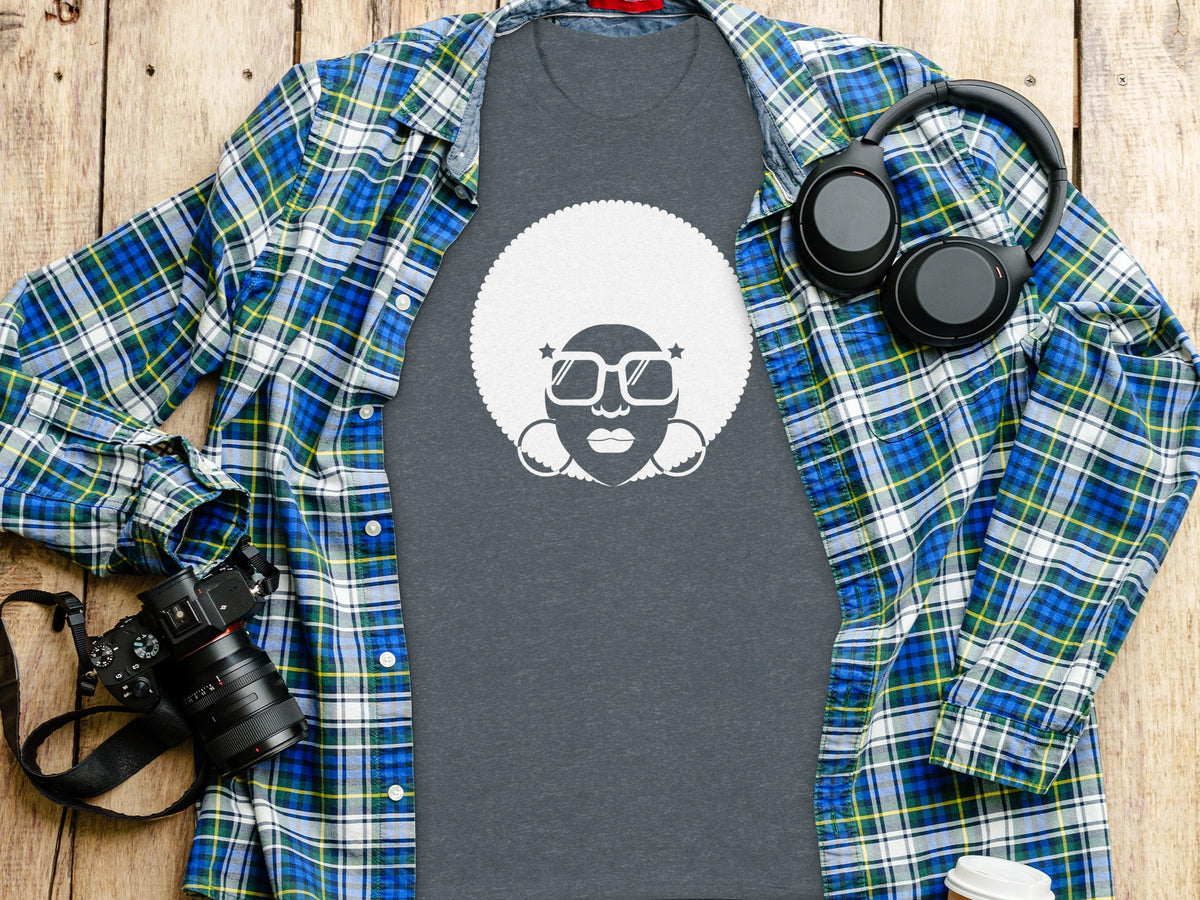 Dark grey t-shirt with white afro-haired person graphic, blue plaid shirt, headphones, and camera.