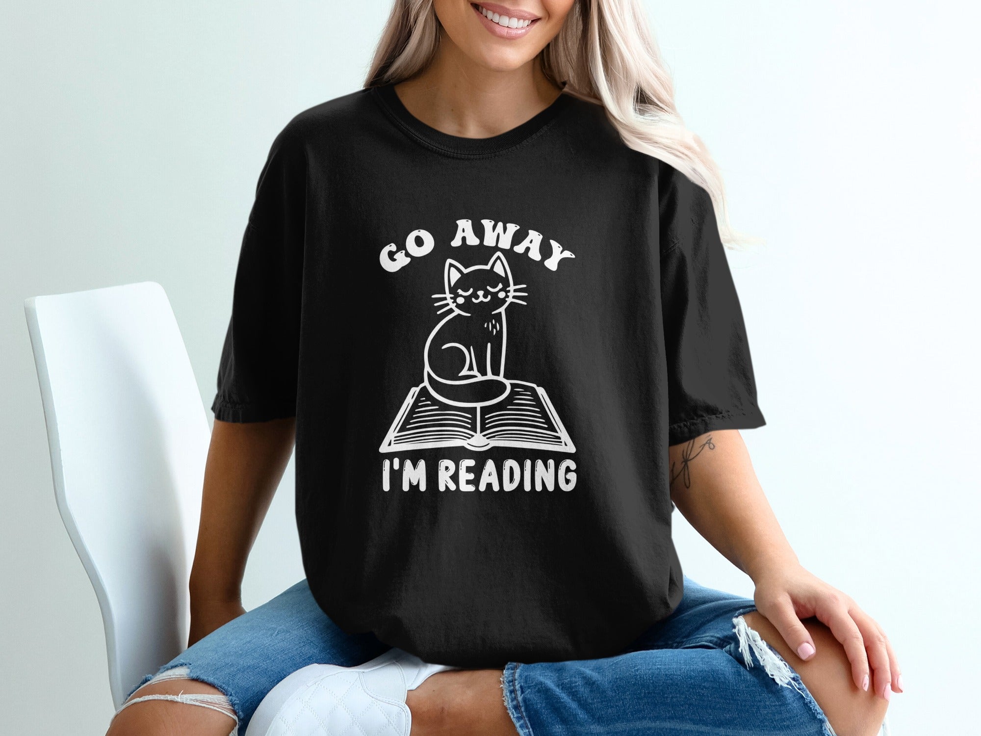 Black t-shirt with white graphic of cat on book, "Go Away I'm Reading".