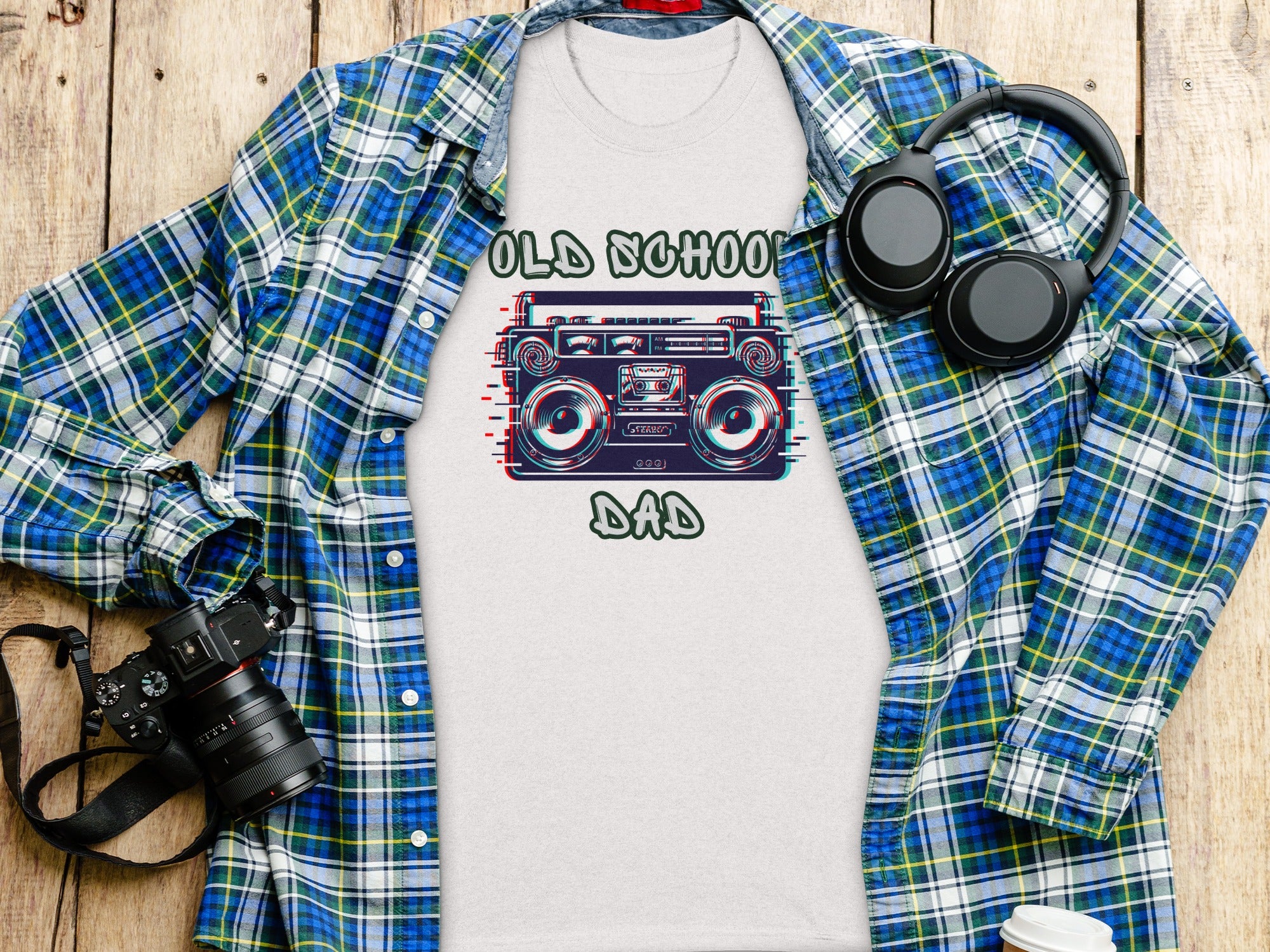T-shirt with "Old School Dad" text and graphic of a boombox, laid flat with a plaid shirt and headphones.