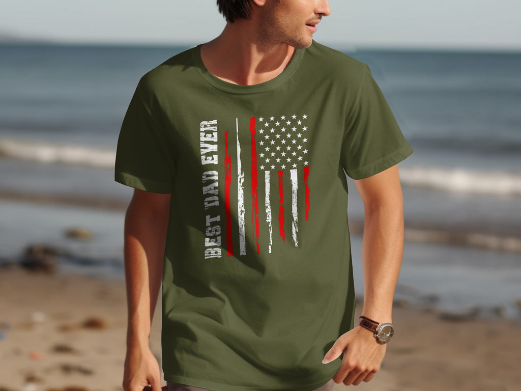 Green t-shirt with distressed American flag and text "BEST DAD EVER" on beach background.