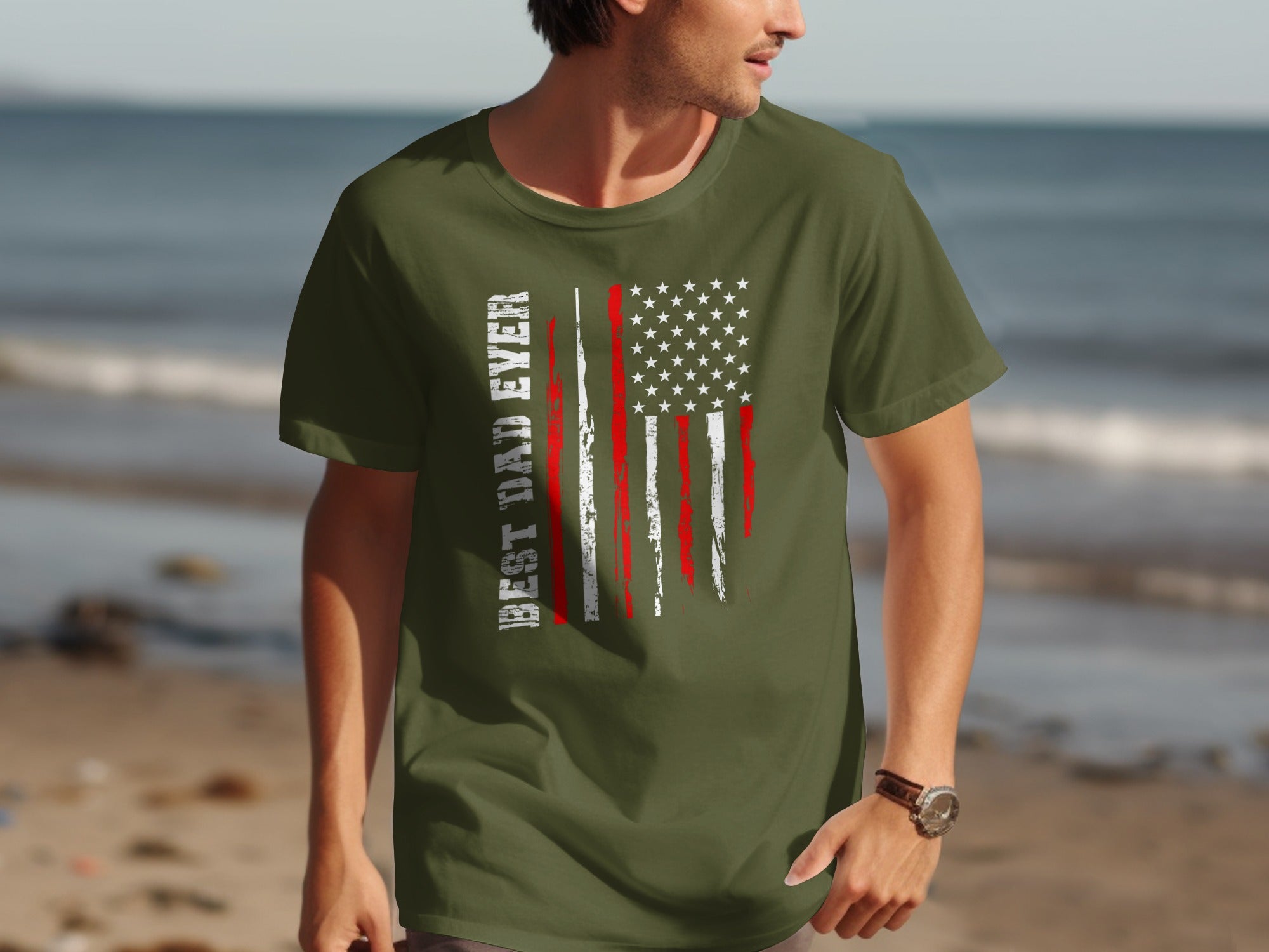 Green t-shirt with distressed American flag and text "BEST DAD EVER" on beach background.