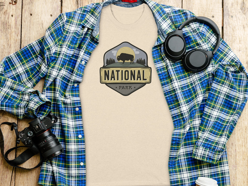 Light tan t-shirt with "National Park" logo, flannel shirt, headphones, and camera.