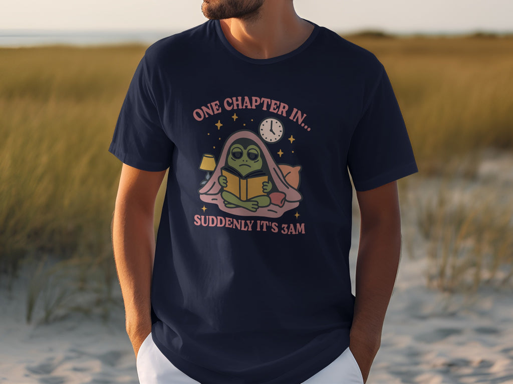 Dark blue t-shirt with graphic of a green alien reading under a blanket with text "ONE CHAPTER IN... SUDDENLY IT'S 3AM".