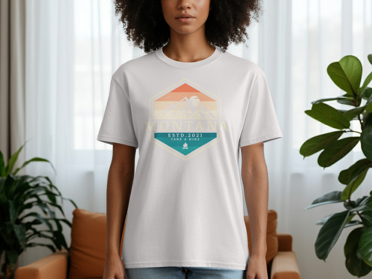 White t-shirt with a hexagonal graphic of mountains, sunset, and text "Montana Estd. 2021 Take a Hike".