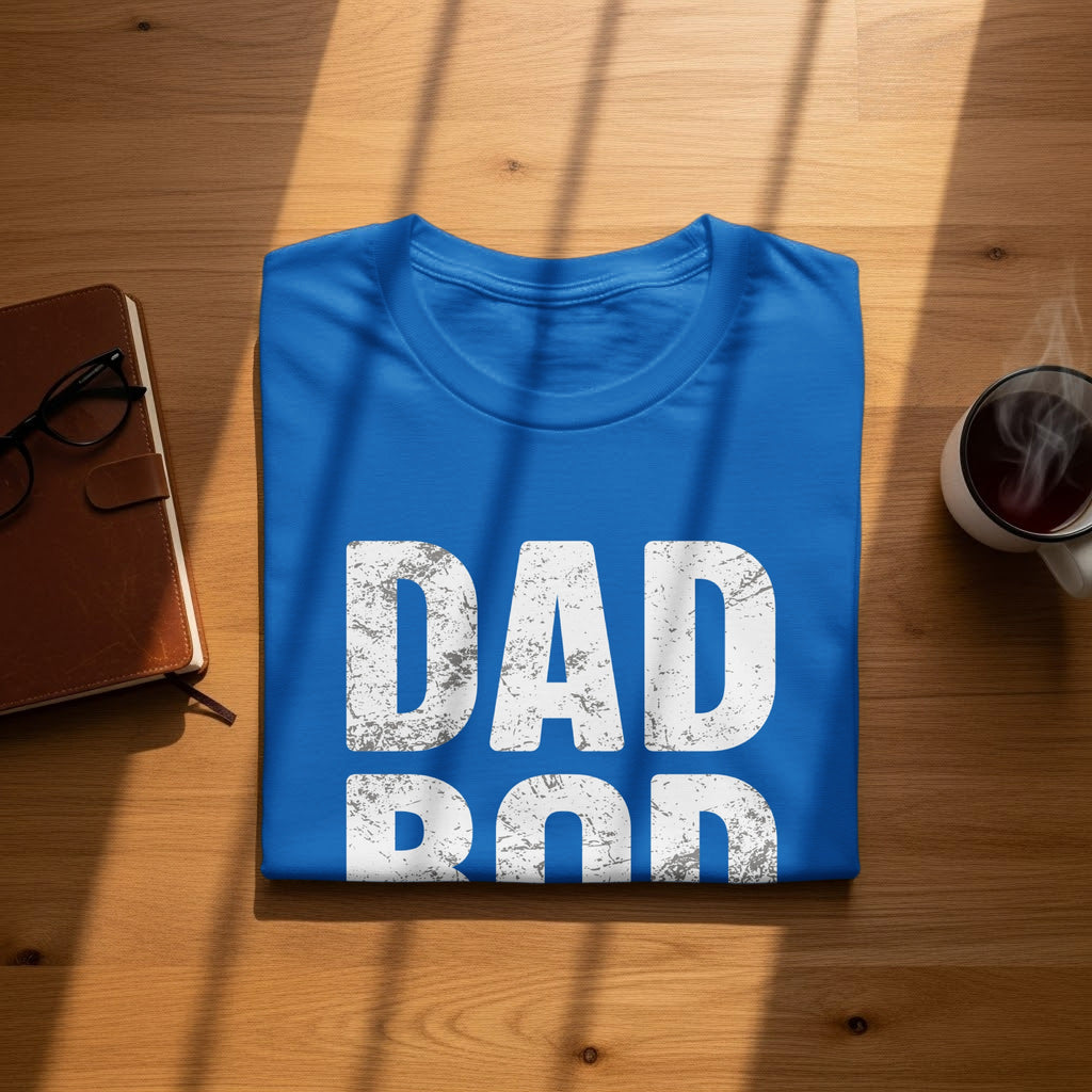 Blue t-shirt with distressed white text "DAD ROD" on a wooden table.