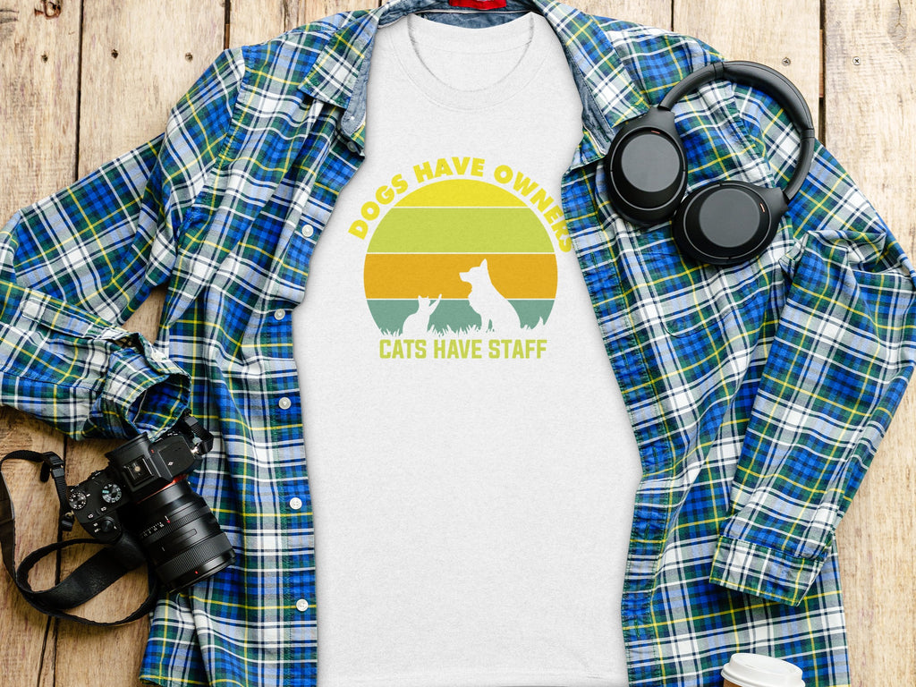 White t-shirt with "Dogs Have Owners Cats Have Staff" graphic and sunset silhouette.