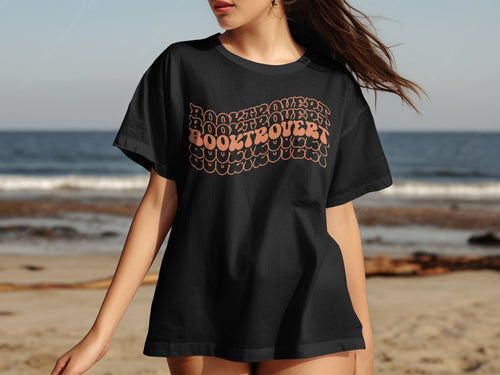 Black t-shirt with curved orange text reading "BOOKTROVERT" on a beach background.