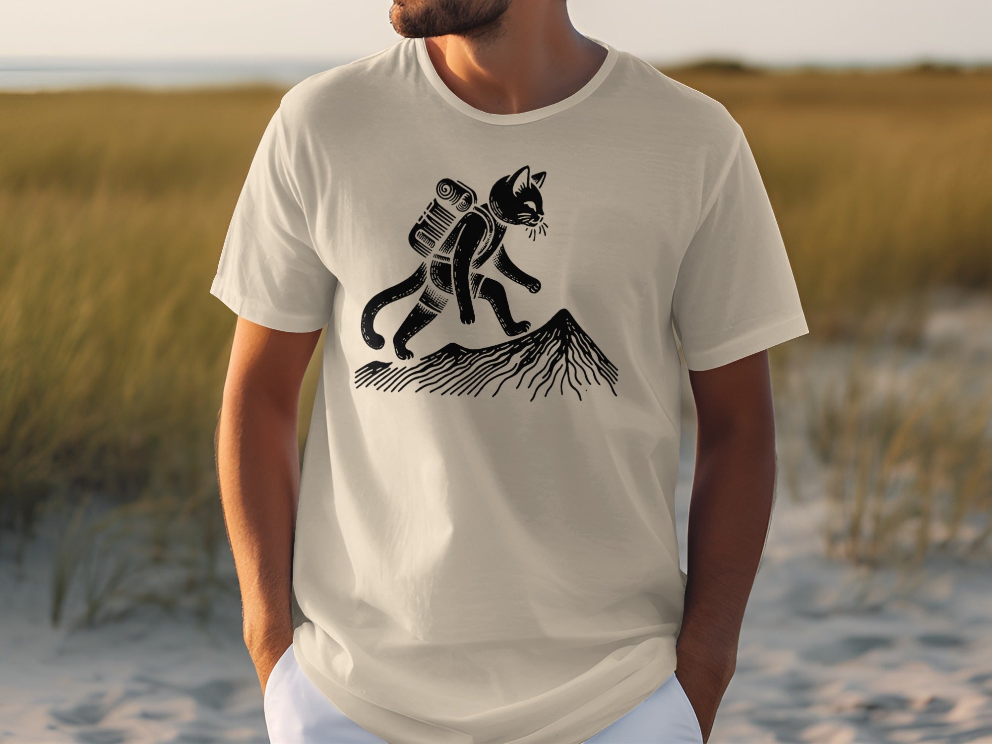 T-shirt featuring a black cat with a backpack hiking up a mountain.