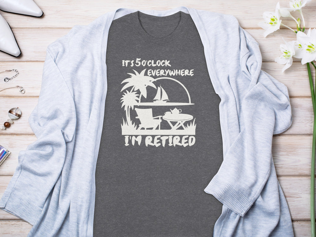 Dark grey t-shirt with white text "It's 5 o'clock everywhere I'm retired" and graphics.