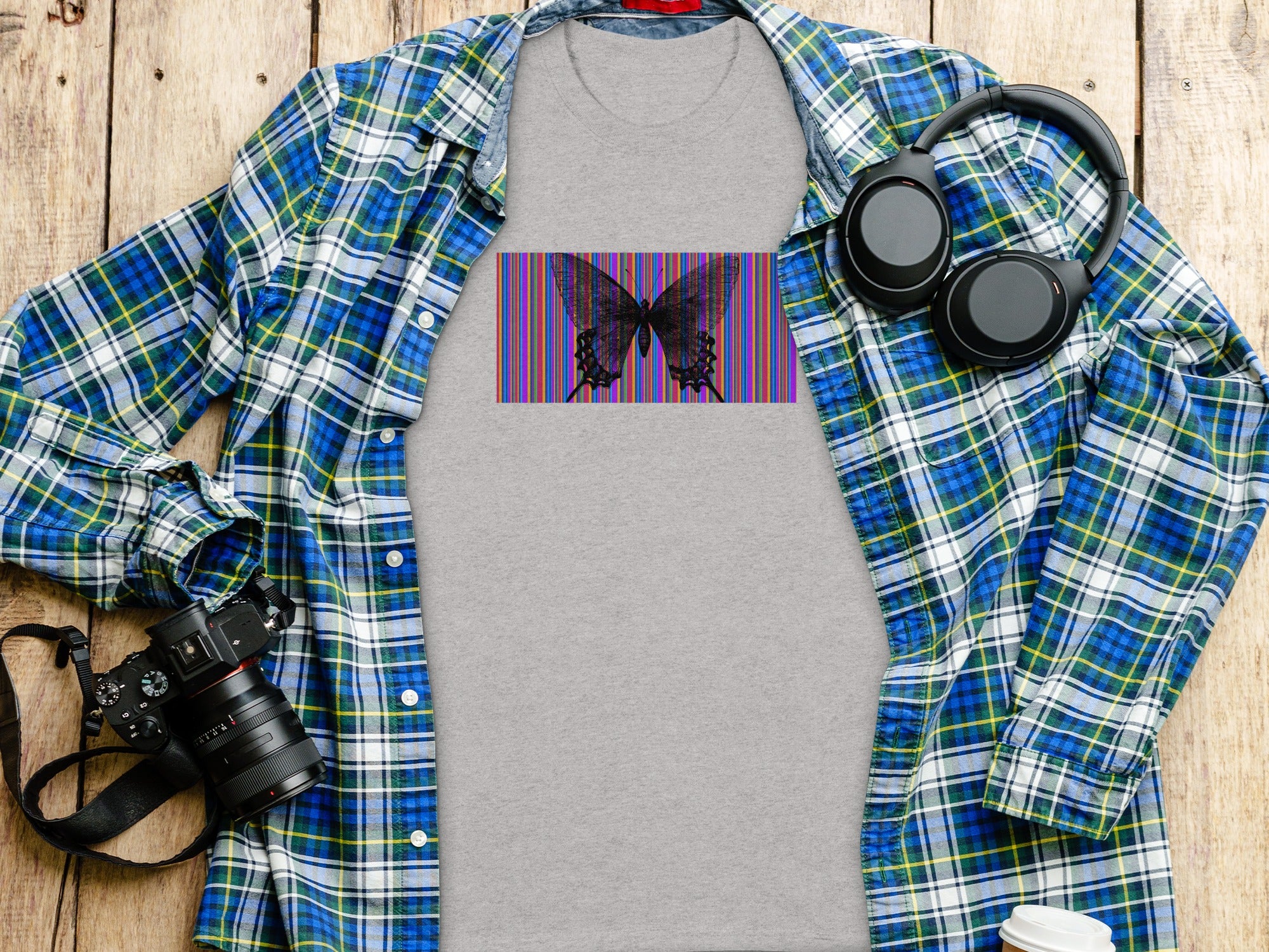 Grey t-shirt with black butterfly and colorful striped graphic on wooden surface.
