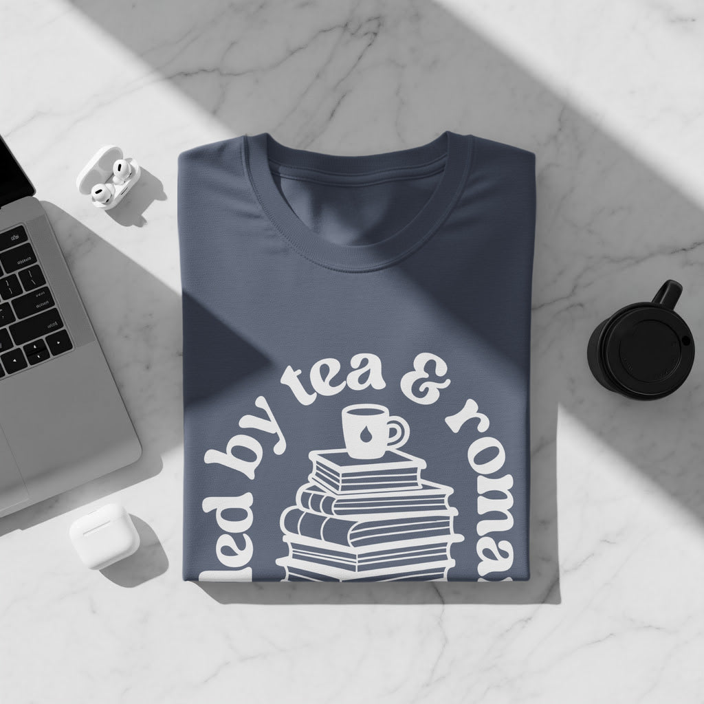 T-shirt with "Led by tea & romance" graphic and stack of books.