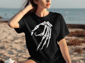 Black t-shirt with white skeleton hand graphic, woman on beach.