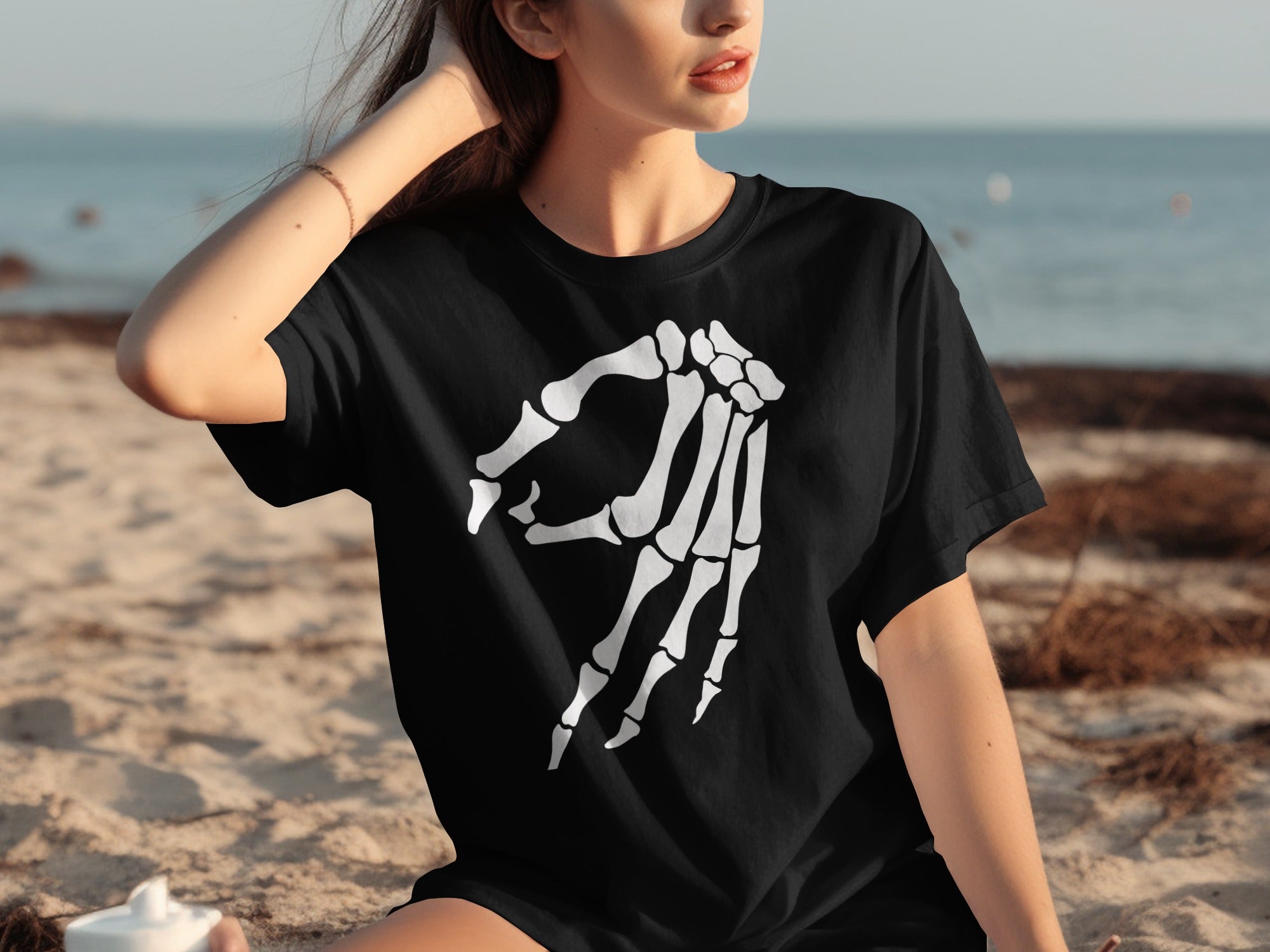 Black t-shirt with white skeleton hand graphic, woman on beach.