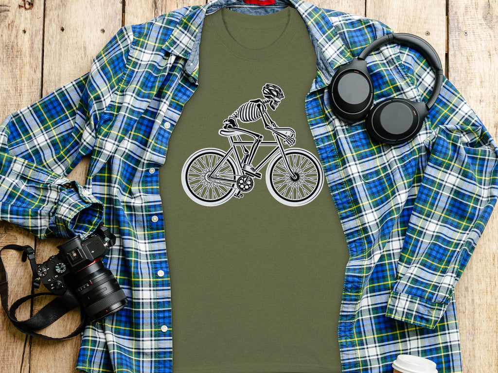 Olive green t-shirt with skeleton cyclist graphic, laid out with plaid shirt and camera.
